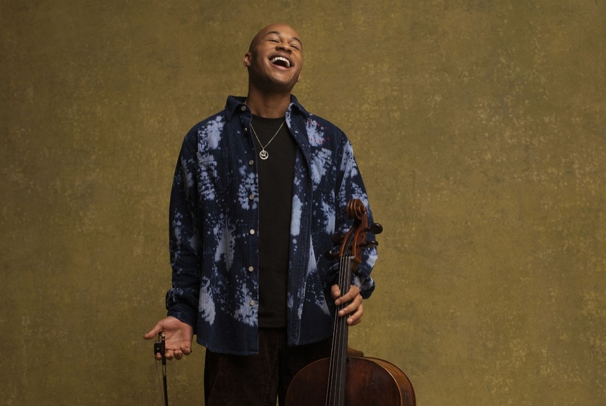 Cellist Sheku Kanneh-Mason, tilting his head back and smiling, holding his cello in his hand.