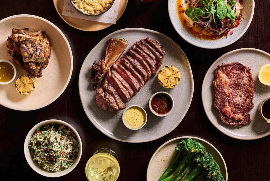 Looking down on a table with many plates, large and small, of meat, veggies and condiments.