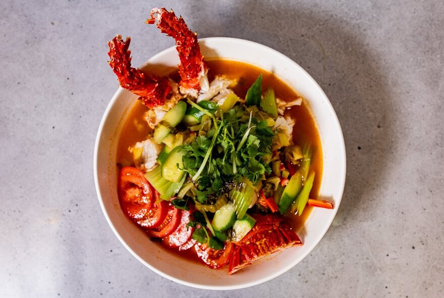 A bowl of seafood in a broth with a chopped green herb garnish on top.