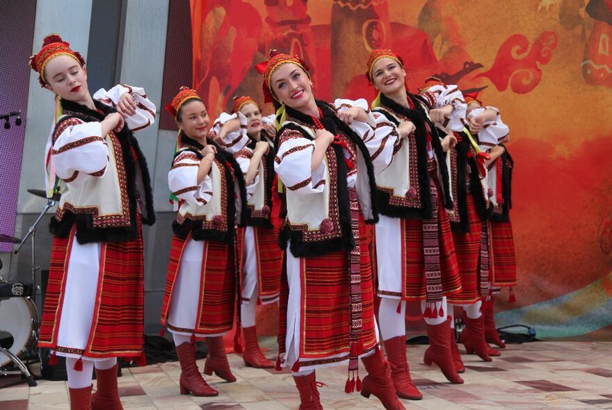 Polish dancers in traditional red, white and black attire, dancing on stage.