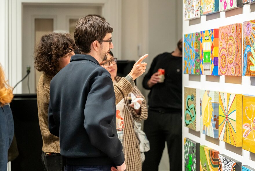People in a gallery interacting while looking at artworks on a wall.