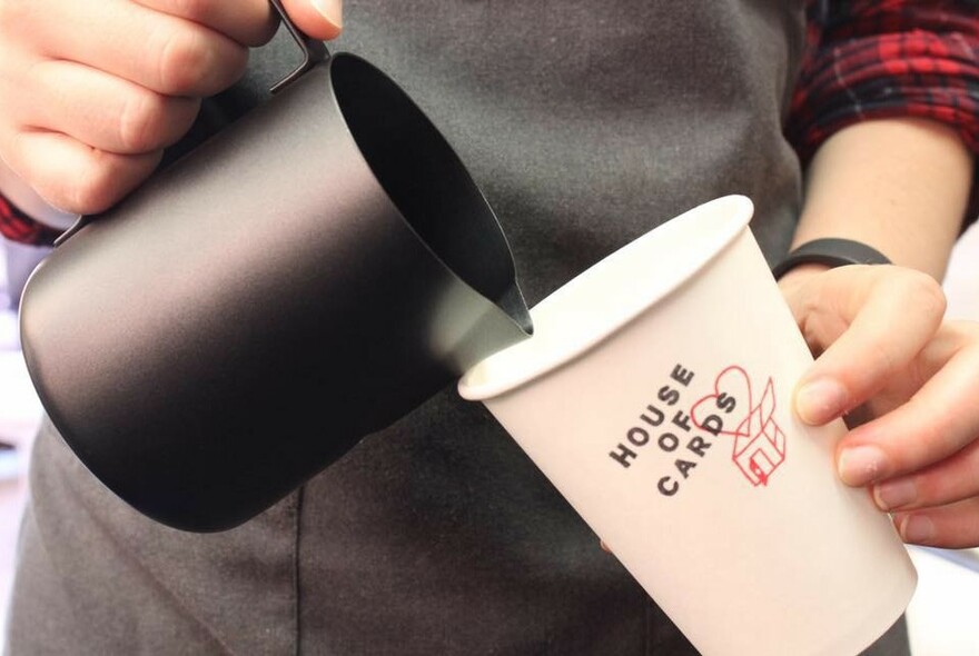 Person pouring from a jug into a takeaway coffee cup.