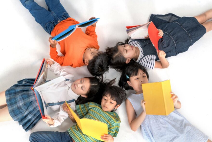 Children lying on the floor reading books, lying head to head in a star shape.