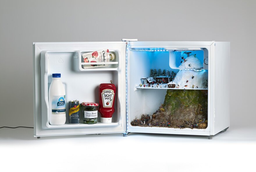 A miniature open fridge sculpture, with objects inside the space.