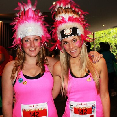 Two women wearing pink singlets with racing numbers and elaborate headdresses. 