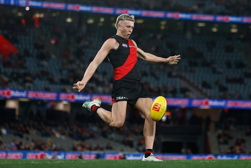 An Essendon football player kicks a ball in front of a crowd.