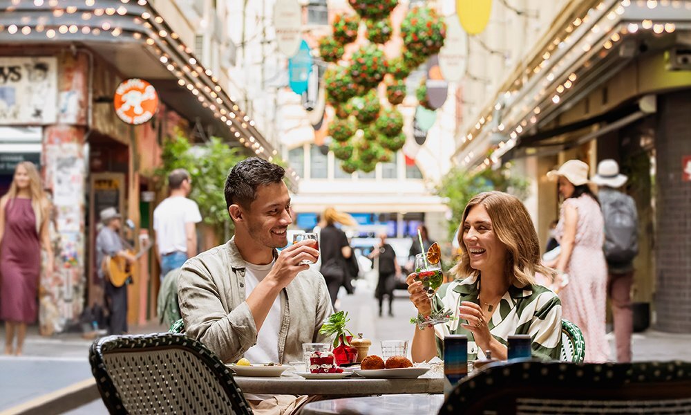 Man and woman drinking cocktails at a table in the middle of a Melbourne laneway.