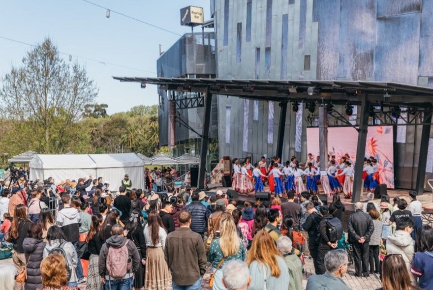 A large group of people standing in Federation Square watching dancers perform. 