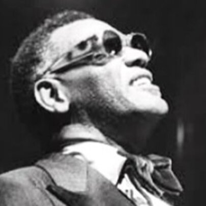 Old black and white photograph of Jazz musician, Ray Charles, wearing a suit and cravat and sunglasses, looking up.