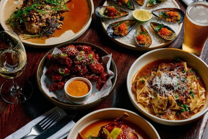 Looking down at a spread of vibrant dishes of food on a wooden dining table inside a restaurant.