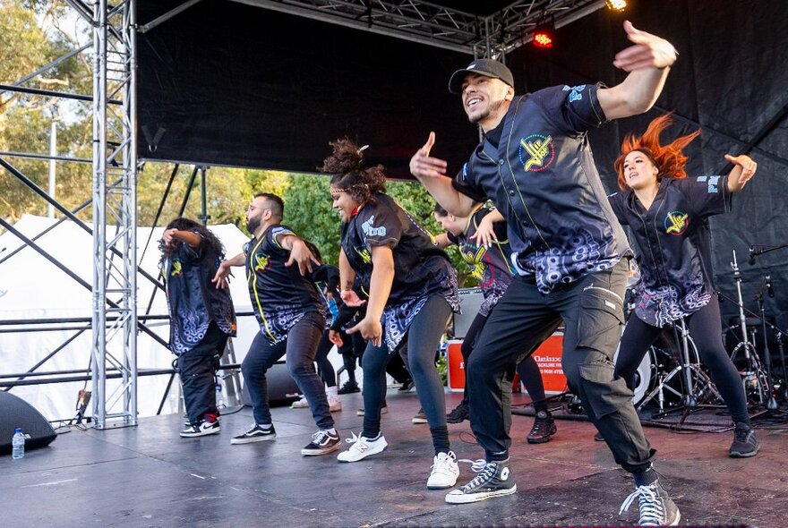 A group of First Nations performers dancing on stage wearing black.