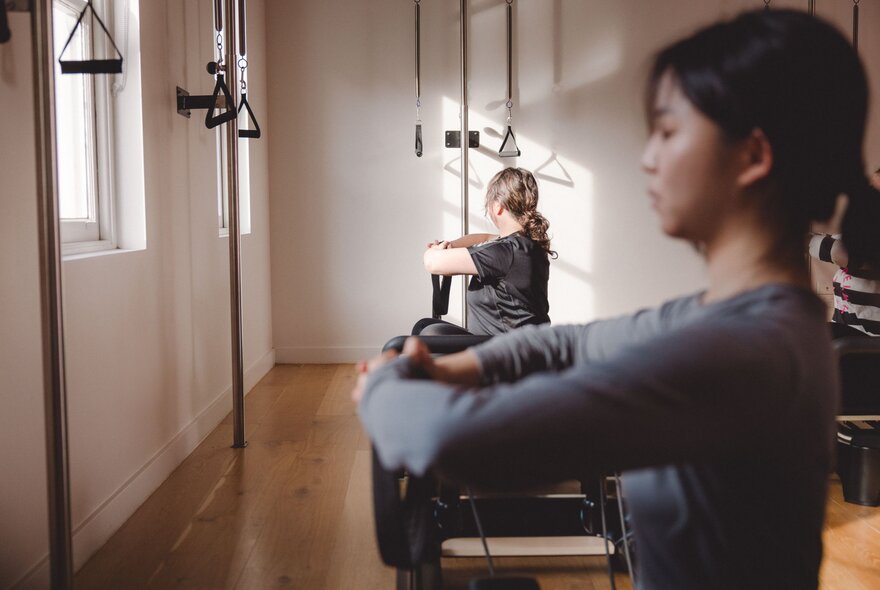 Two women in a Pilates studio posing with arms up. 