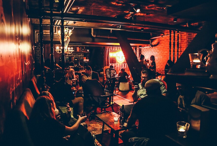 Lots of people sitting at tables in a dark, crowded red-lit bar.