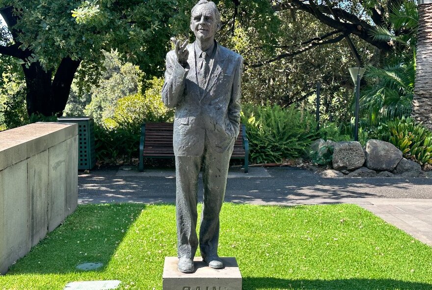 A bronze statue of a man, on a patch of green grass in a park in East Melbourne.