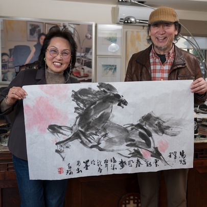 Two artists holding up a Chinese ink artwork of a horse.
