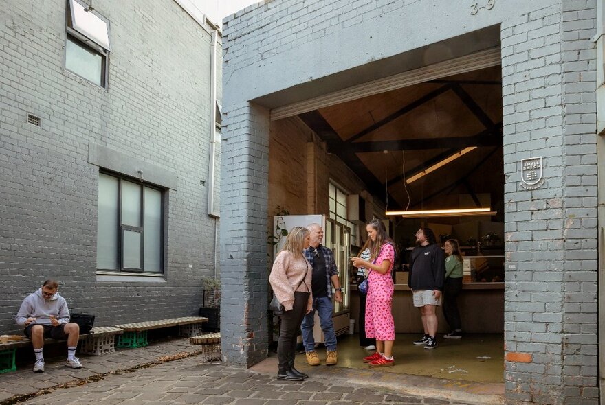 An outdoor courtyard and garage entrance to a brick warehouse building with several people standing around and chatting.