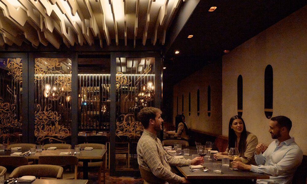 Three friends at a restaurant with a geometric light installation on the ceiling.