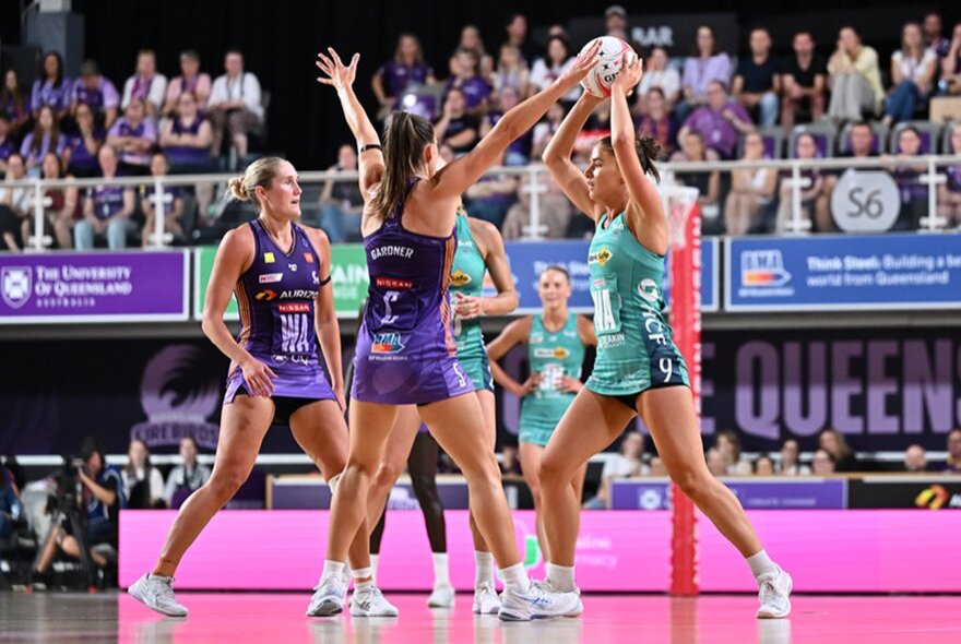 Women's netballers during a game, players in purple trying to get the ball from players wearing teal.