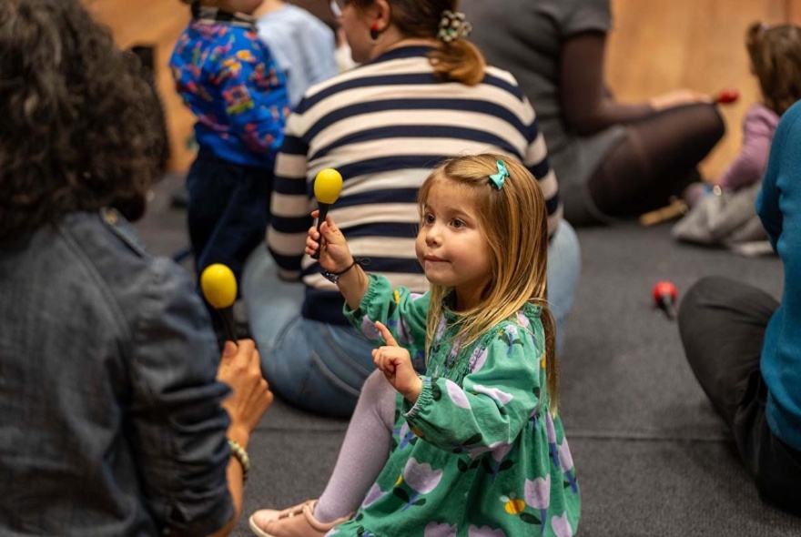 Children and parents seated on the floor, playing with rattle percussion instruments.