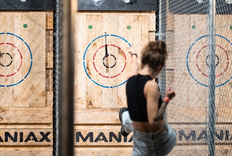 A woman looking at her shot as an axe hits a bullseye.