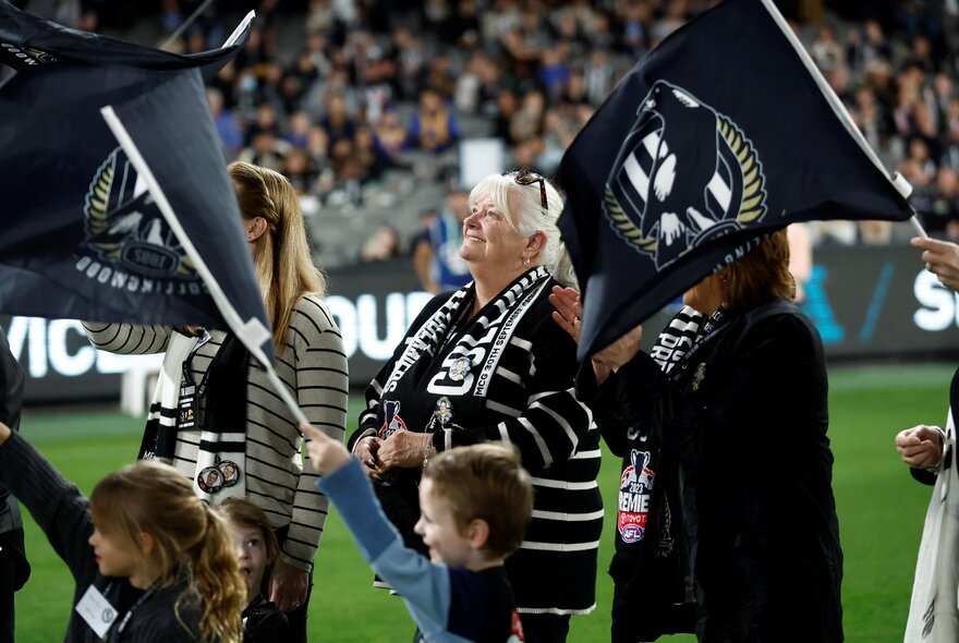 Members of the Collingwood AFL cheer squad on the field holding banners and waving flags.