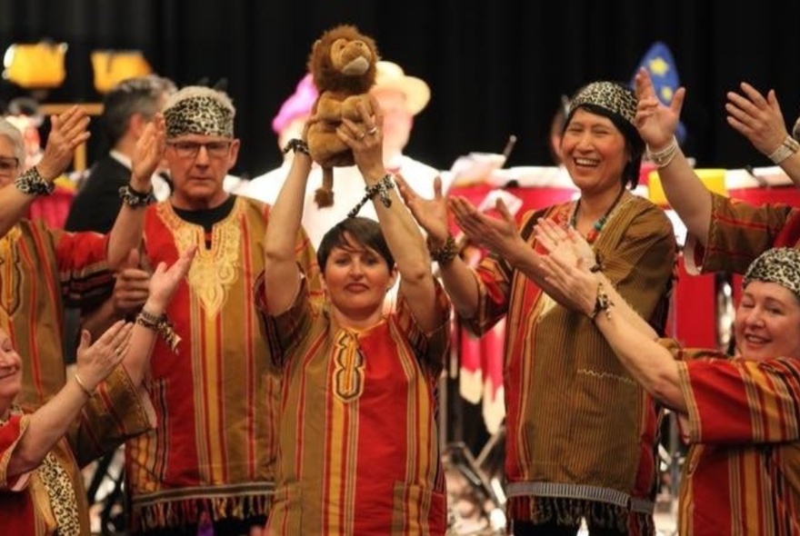 Singers wearing African outfits, the central figure holding a toy lion above their head.