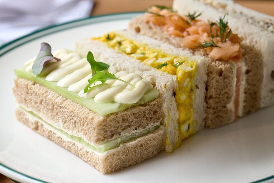A mix of dainty finger sandwiches on a white plate, as part of a high tea dining event.