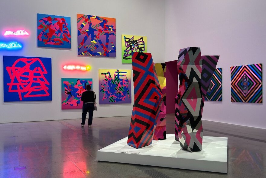 A woman looking at a display of neon art pieces in a gallery.