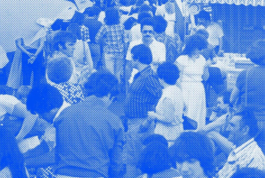 Blue-toned image of people at a community market with stalls.