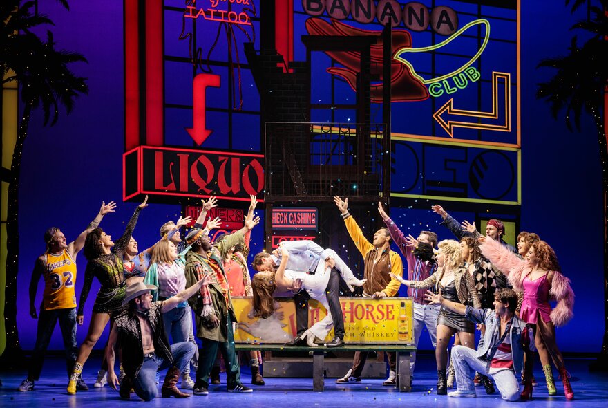 The ensemble cast singing and dancing on a theatre stage during a performance of Pretty Woman: The Musical.