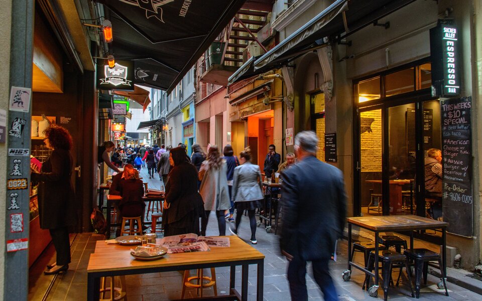 People walking down a busy Melbourne laneway with outdoor dining tables and chairs.