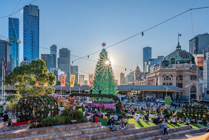 Fed Square busy during the day with people milling around a large green Christmas tree.