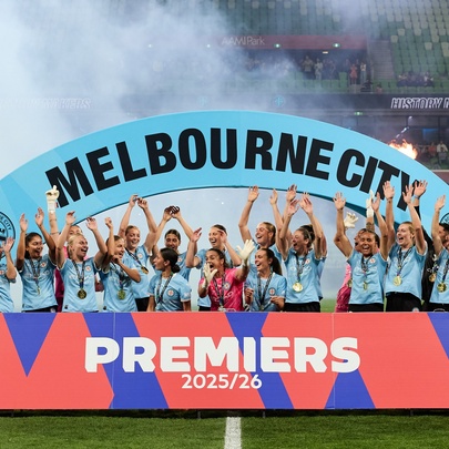 Women's soccer team standing behind a banner with arms raised in the air.