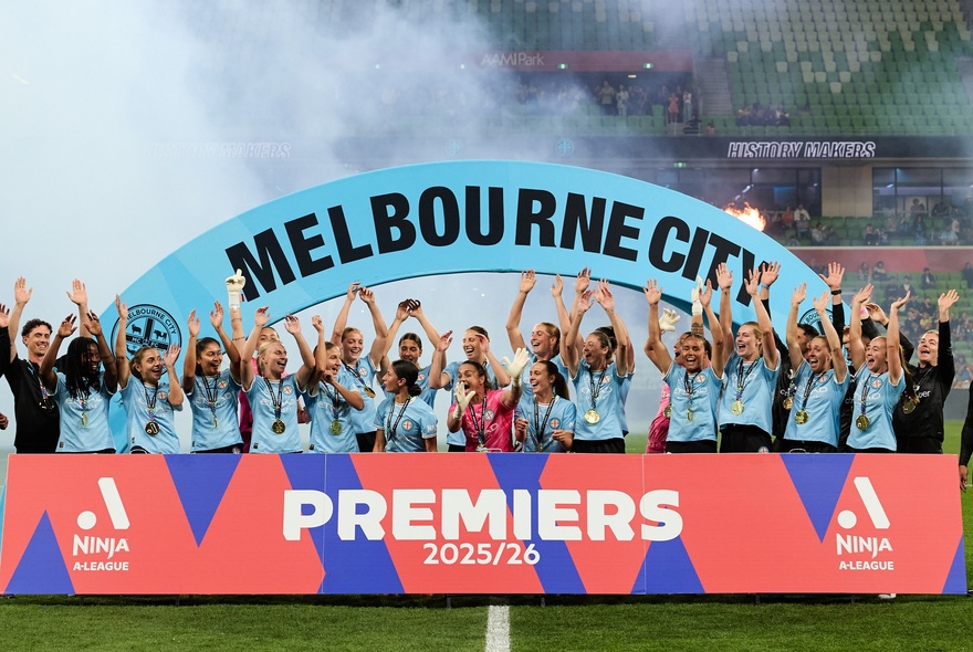 Women's soccer team standing behind a banner with arms raised in the air.