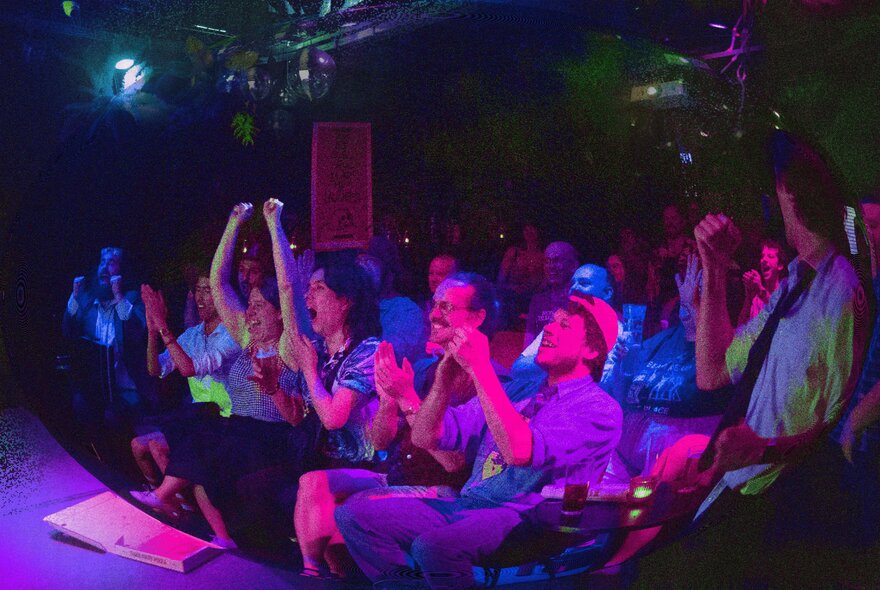 A seated audience in a small club, reacting enthusiastically to a stand-up comedy show. 