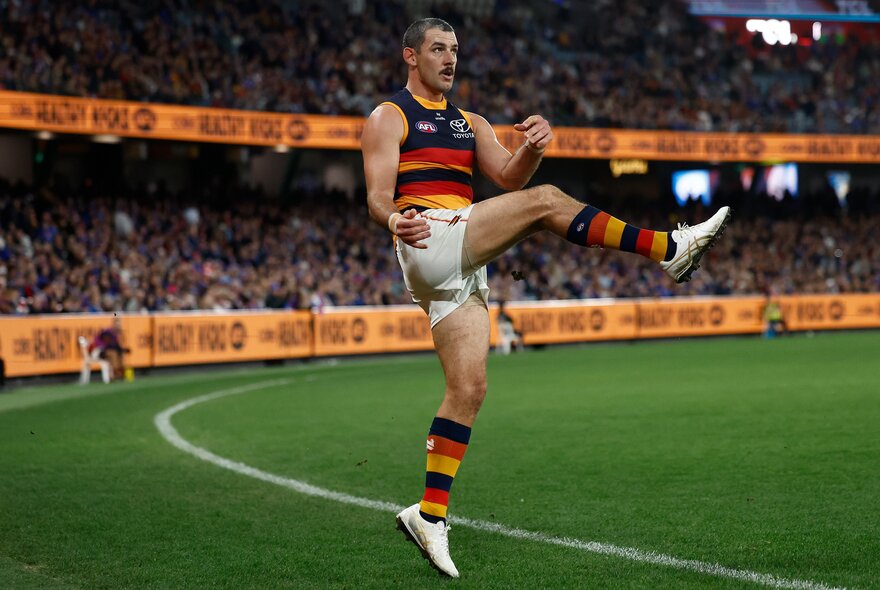 An Adelaide Crows player kicks a ball from behind the boundary line during match. 