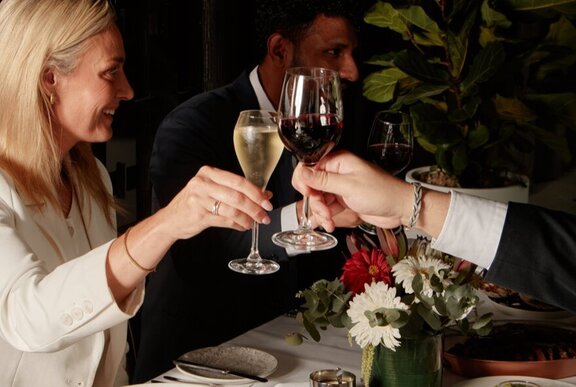 Woman with blonde hair clinking glasses at a table.