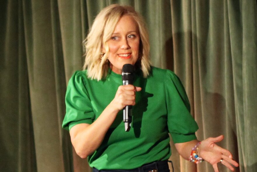 Comedian Claire Hooper, wearing a green top and taking into a microphone on a stage.