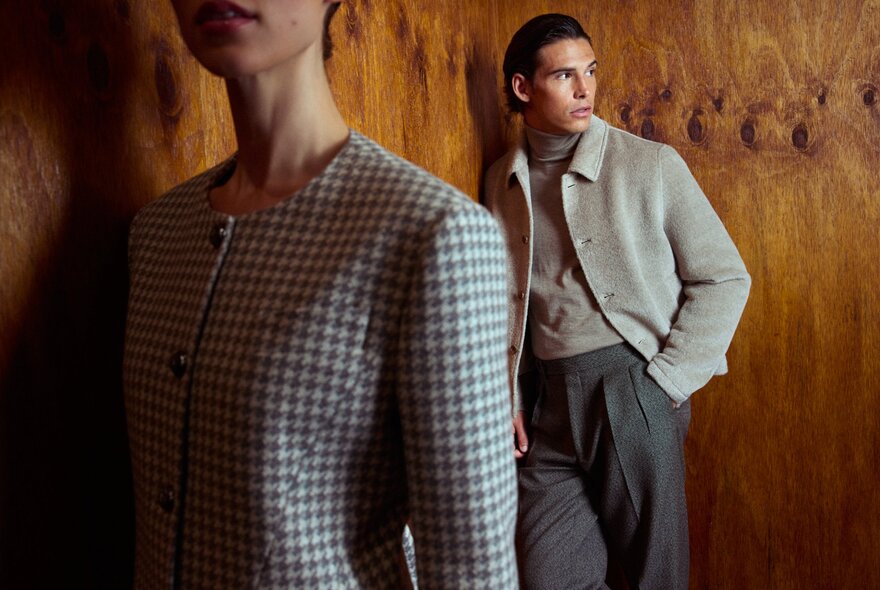 Two models, one wearing a checked jacket standing in the foreground, and one in the background wearing tailored trousers, and a casual jacket.
