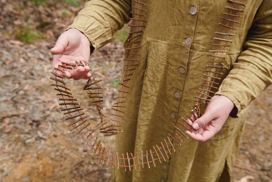 Hands holding forth a long necklace that looks like railway tracks. 