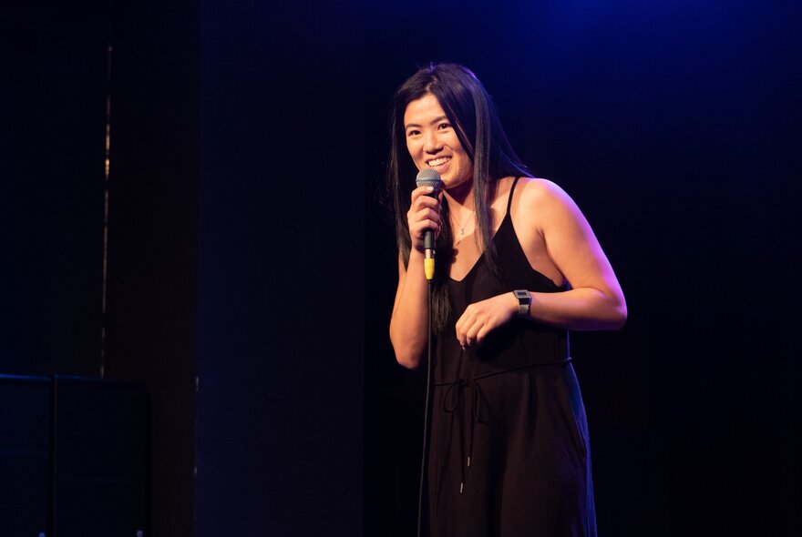 Performer wearing black in a dark venue, holding a microphone.