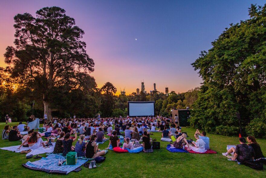 People watching a movie in a park at sunset. 