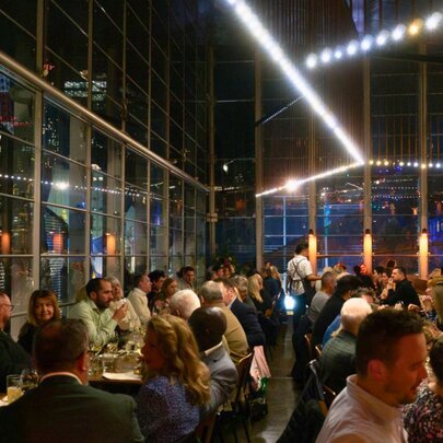 Airy dining space at Taxi Kitchen, at night, with the dining space filled with patrons seated at tables eating and drinking.
