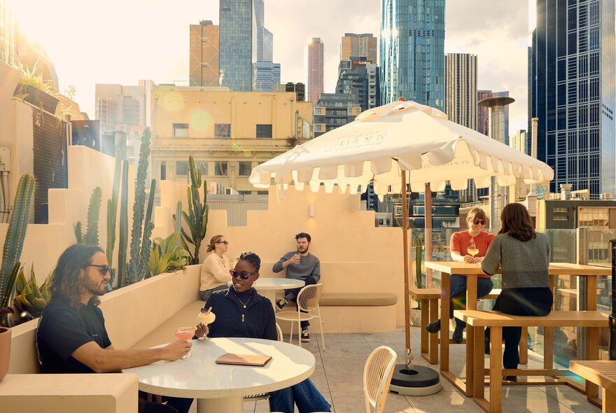 A group of people are enjoying cocktails in the sun on a rooftop bar.