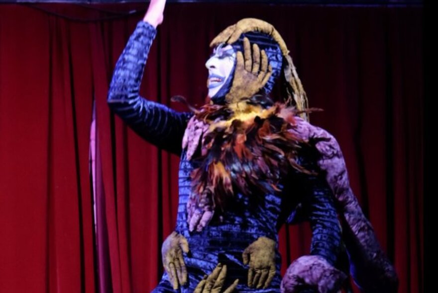 Drag performer wearing white and purple makeup and catsuit.