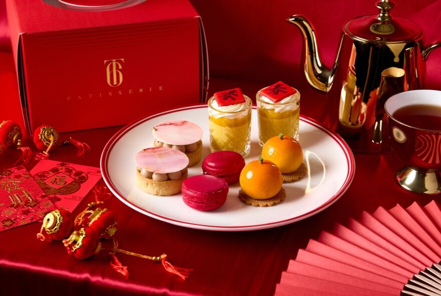 Afternoon tea selection of pastries and desserts on a plate against Chinese New Year red background with fan and ornaments.