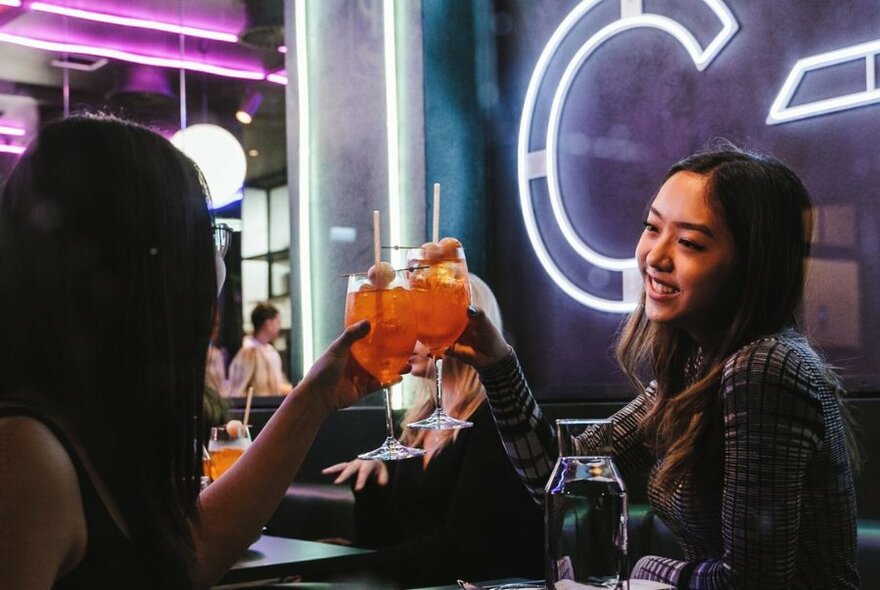 Two people seated at a bar, clinking glasses of orange drink.