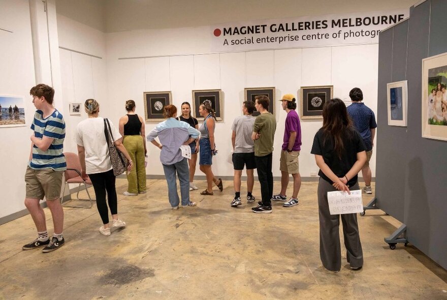 People walking around inside Magnet Galleries and viewing a photographic exhibition displayed on the walls.