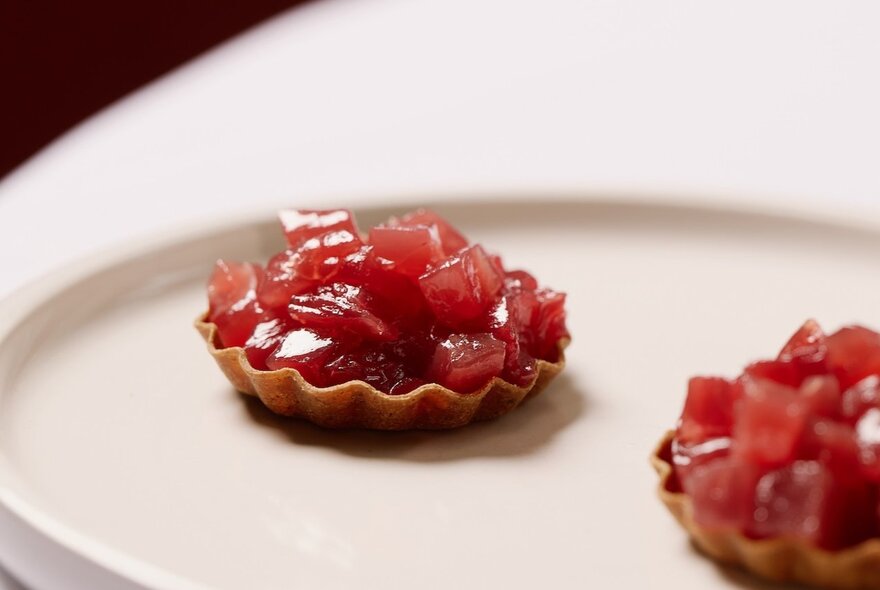 Two mini pastry tarts with a red filling on a white plate.