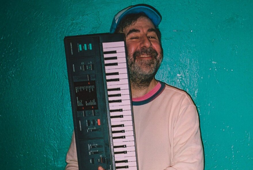 Smiling man with beard and cap holding a keyboard.